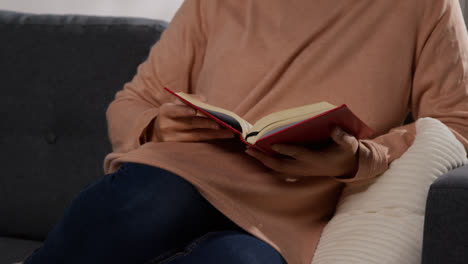 Close-Up-Of-Muslim-Woman-Sitting-On-Sofa-At-Home-Reading-Or-Studying-The-Quran
